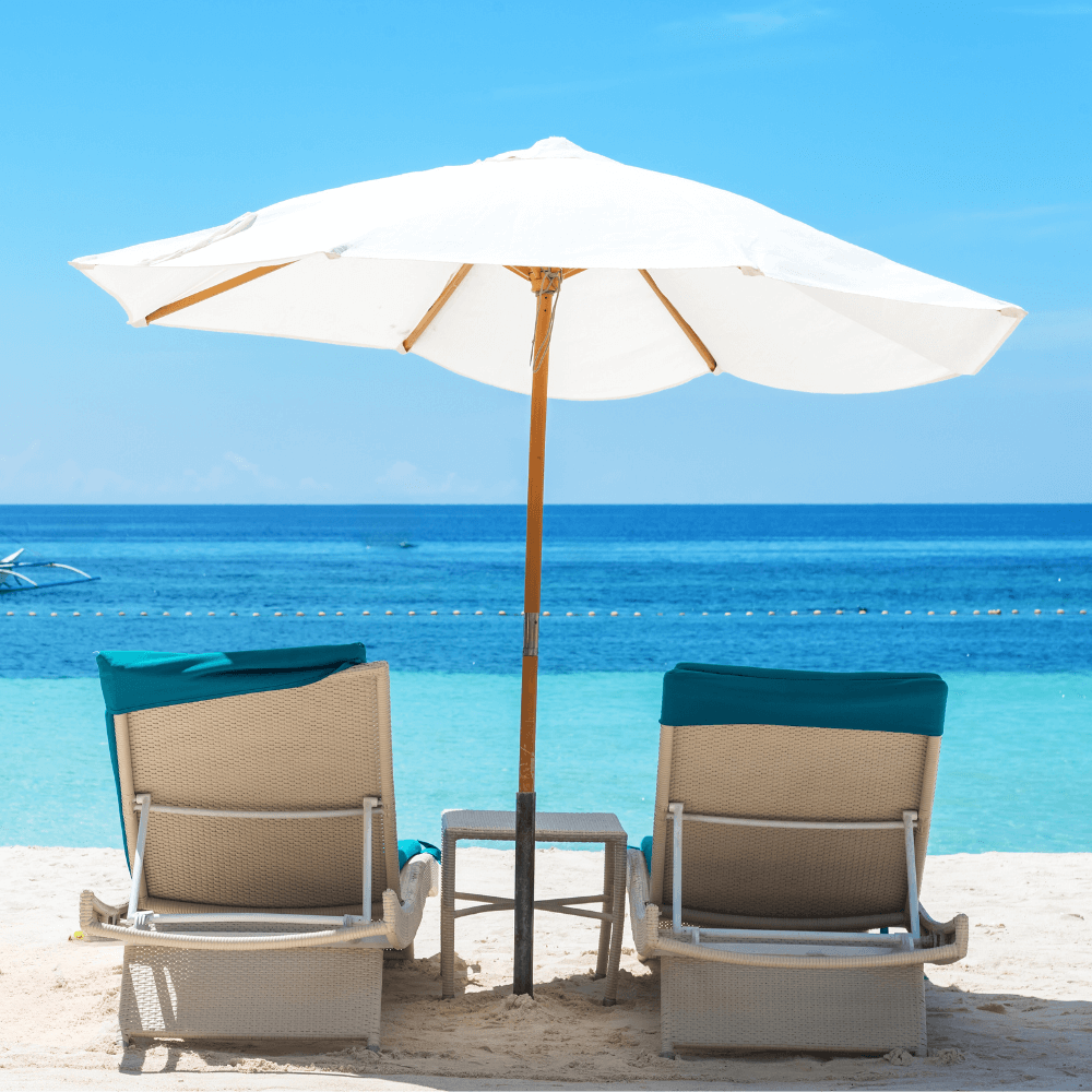 Wit strand met twee ligbedjes en een witte parasol. En een helder blauwe zee op de achtergrond.